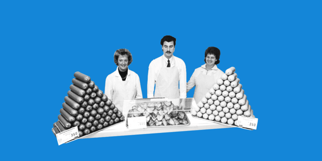 Drei Personen in weißen Kitteln stehen hinter einer Verkaufstheke, links und rechts je eine Pyramide aus gestapelten Würsten mit Preisschildern