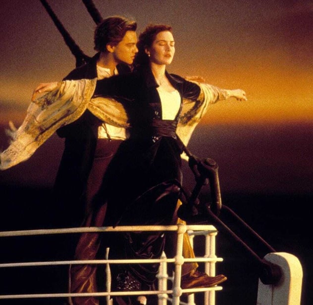 Jack und Rose an der Bugreling der Titanic mit ausgebreiteten Armen vor Abendhimmel – der Moment kurz vor der Kollision mit dem Eisberg