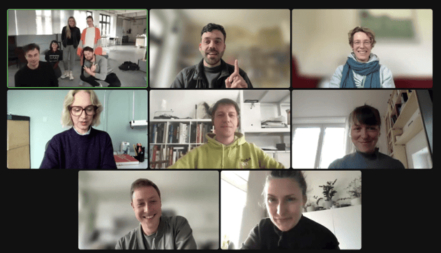 Videokonferenz mit neun Kacheln: acht einzelne Teilnehmende zu Hause und eine Kachel mit einer Gruppe im Büro, alle lachend