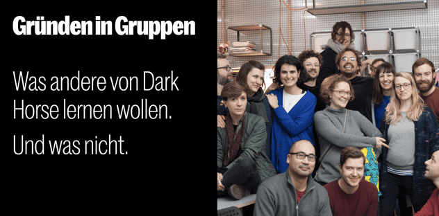 Gruppenfoto: rund fünfzehn lachende Menschen dicht beieinander in einem Loft-Büro