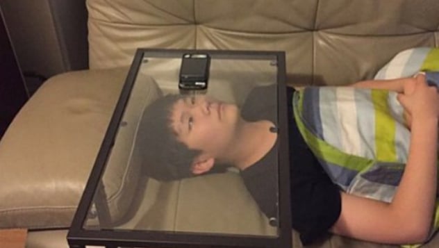 Nutzer liegt auf einem Sofa und hat sein Smartphone auf einen umgedrehten Glastisch über seinem Gesicht gelegt, um es nicht halten zu müssen