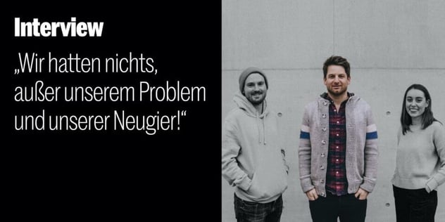 Drei junge Menschen in Pullovern und Strickjacke stehen lächelnd vor einer Betonwand, schwarzweiß