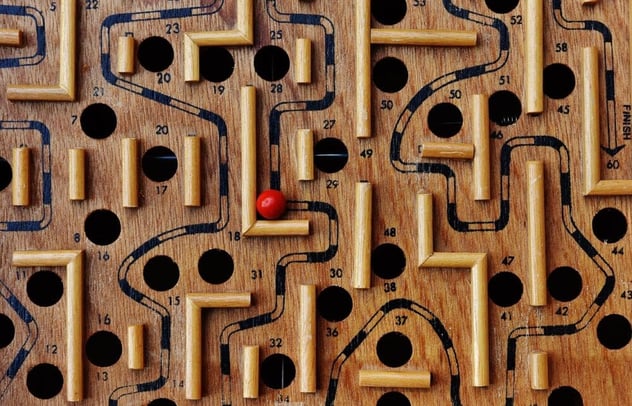 Hölzernes Kugellabyrinth mit nummerierten Löchern und aufgezeichnetem Pfad bis zum Feld „Finish“; die rote Kugel steht auf halber Strecke zwischen zwei Barrieren