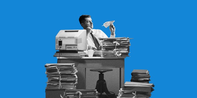 Freigestellte Schwarz-Weiß-Collage eines Verwaltungsmitarbeiters an einem Schreibtisch voller Aktenstapel, vor blauem Hintergrund